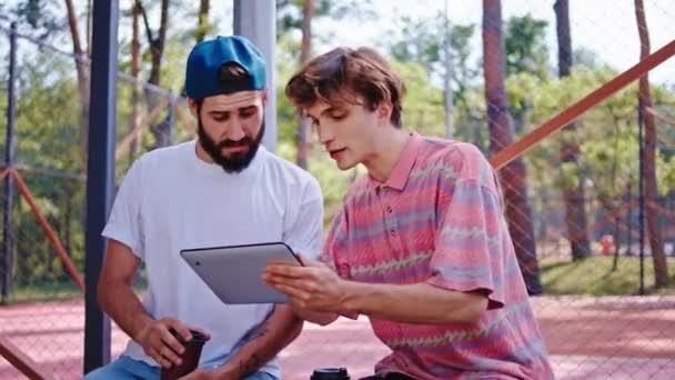 Fechar-se para a câmera dois bons amigos caras em um parque moderno usando um tablet eletrônico para estudar juntos eles analisam algo concentrado. Tiro em ARRI Alexa Mini — Vídeo de Stock