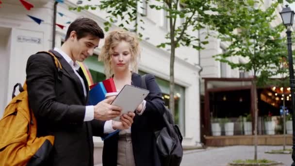 Hermosa mujer con una gran sonrisa tienen una conversación amistosa con su colega hombre de la oficina que echan un vistazo a la tableta electrónica y sonriendo juntos en medio de la calle — Vídeos de Stock