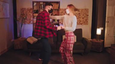 Karantina konsepti COVID-19 'da pijama ve koruyucu maskeyle dans eden yakışıklı çift.