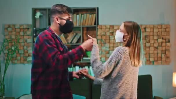 A sötét nappaliban boldog karizmatikus táncos pár védő maszkkal töltik az időt a karanténban Covid-19 — Stock videók