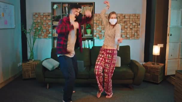 En la cuarentena en casa pareja muy emocionada bailando llevaban máscara protectora sintiéndose genial en pijamas COVID-19. 4k — Vídeo de stock