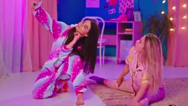 In front of the camera charismatic two young women in the bedroom down on the carpet take some pictures in a funny pajamas they have a good girls night — Stock Video