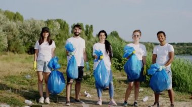 Güneşli bir günde, kameranın önünde, büyük bir gölün yanında, kameranın önünde mavi plastik poşetlerle poz veren çok ırklı gönüllülerden oluşan bir plaj grubunun yanında. ARRI Alexa Mini 'de çekilen