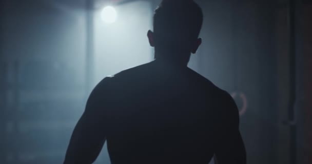 Bodybuilding kille med en perfekt kropp i en i den mörka gym klassen tar video från ryggen han börjar träna hårt — Stockvideo