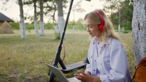 Bella giovane donna con i capelli biondi nel parco sedersi sull'erba ha una discussione attraverso il computer portatile un'intervista di lavoro si concentrò con un bel sorriso spiegando qualcosa. 4k — Video Stock