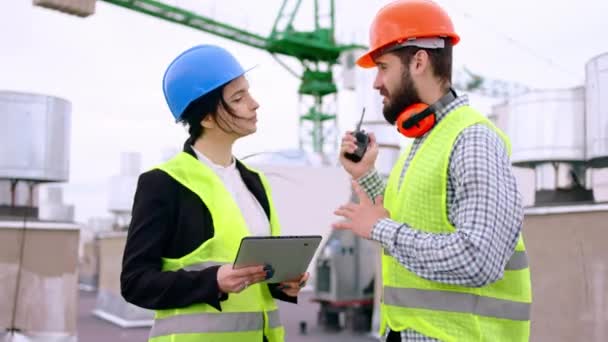 Moderno canteiro de obras no topo do edifício carismático mulher engenheiro e construtor principal homem com um capacetes de segurança começar a caminhar através do canteiro de obras analisando o plano — Vídeo de Stock