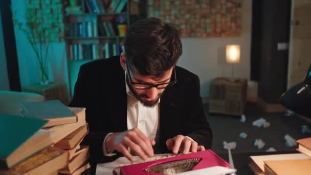 Koncentrerad man med glasögon i biblioteket tittar rakt mot kameran talar med uttryck sedan fortsätter han att skriva något på sin skrivmaskin — Stockvideo