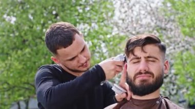 Kameranın önünde berber için mükemmel güneşli bir gün. Bir erkeğe profesyonel saç tıraşı yapmak için elektronik makas kullanıyor. ARRI Alexa Mini 'de çekilen