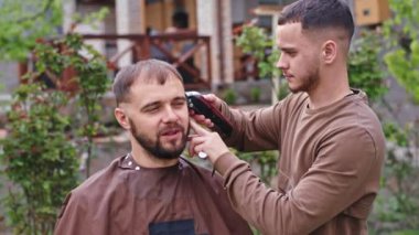 Evdeki bahçedeki yakışıklı adamın saç kesimi konusunda uzman berber, saç makasını kullanıyor.