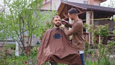 İyi görünümlü arkadaşlar bahçede saç kesiciyle saç kesiyorlar Coronavirus 'un karantinasında.