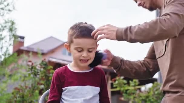 Przystojny facet skończyć profesjonalną fryzurę do swojego młodszego brata w ogrodzie on wziąć szczotkę do czyszczenia wszystkich włosów z szyi — Wideo stockowe