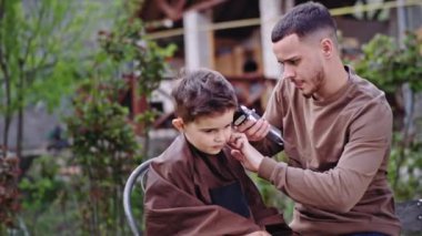 Bahçedeki berber şirin ve komik küçük bir çocuğa saçını kestirir. Sandalyede oturur ve saçını kestirmesini bekler.