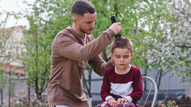 Acasă în grădină carismatic băiețel mic face un om de frizer profesionist tăiat părul folosind tăietorul de păr în carantină Covid 19 — Videoclip de stoc