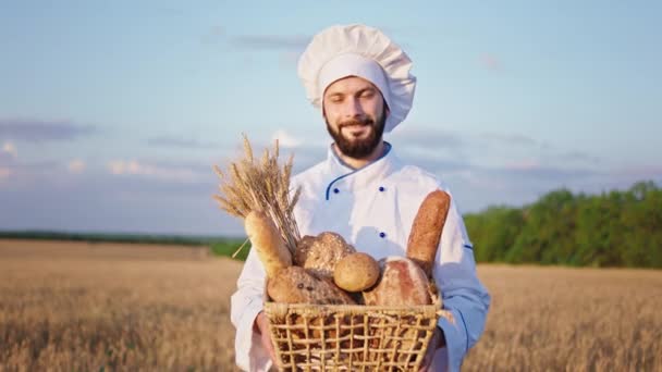 Concepto de agricultura panadero hombre sosteniendo una gran cesta de pan recién horneado y sonriendo a lo grande a la cámara que están en el medio del campo de trigo — Vídeo de stock
