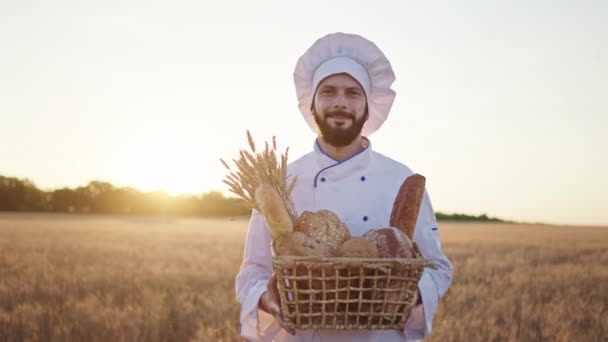 Uomo carismatico panettiere in mezzo al grano in possesso di un grande cesto di un pane fresco e sorridente carino davanti alla fotocamera — Video Stock