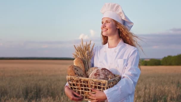 Samice pekařka velmi atraktivní s dlouhými kudrnatými vlasy drží košík plný přestávky uprostřed pšeničného pole. Shot na ARRI Alexa Mini. — Stock video