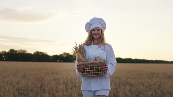 カメラの女性のパン屋の前を歩くと、新鮮なパンが小麦畑の真ん中にバスケットを保持しています — ストック動画