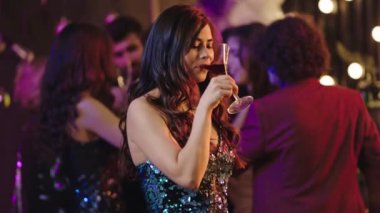 Kameranın önünde, partide gülümseyen, kokteyl içen ve gecenin tadını çıkaran karizmatik bayan kameraya bakıyor.