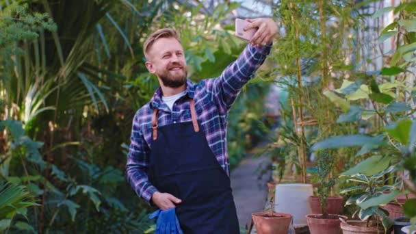 Przystojny człowiek ogrodnik zrobić zdjęcie z jego smartfon on uśmiechając się duży podczas mieć przerwę w środku rolnicze szklarnia — Wideo stockowe