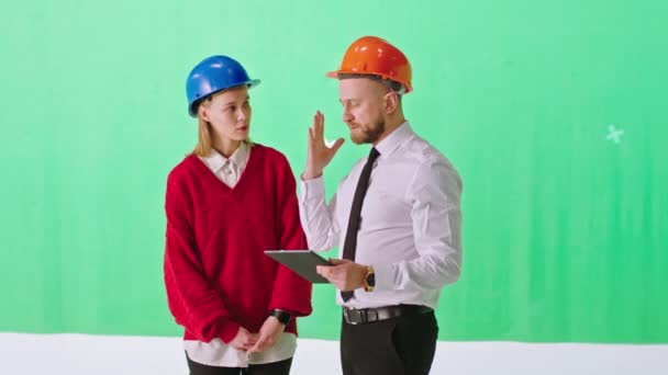 大型绿色工作室一位漂亮的女士和迷人的男人头戴安全帽，用平板电脑讨论施工计划 — 图库视频影像