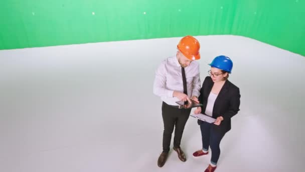 Зеленая студия красивая ассистентка и бизнесмен анализируя стройплощадку они носят защитные шлемы с помощью цифрового планшета для плана — стоковое видео
