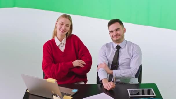 Atractivo chico y rubia dama de pelo posando delante de la cámara mientras se sientan en las sillas que sonríen grandes en un estudio de croma key — Vídeos de Stock