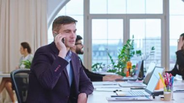 İş gününün ortasında panoramik ofis kameranın önünde ana yönetici telefonda konuşuyor diğer ofis çalışanları bir şey tartışıyor