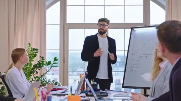 Atraktivní chlap s brýlemi mají schůzku se svým týmem v kanceláři, které společně analyzují statistiku obchodního plánu chlap reprezentující na tabuli výsledek statistiky — Stock video