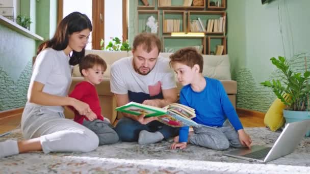 Fique em casa na sala de estar jovem família todos juntos no chão lendo um livro de história eles são muito felizes passar o tempo juntos — Vídeo de Stock