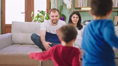 Harika görünümlü ebeveynler güzel çocuklarıyla vakit geçiriyorlar kanepede oturup birbirlerine sarılıyorlar ve aileleriyle birlikte anın tadını çıkarıyorlar.