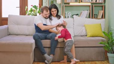 Genç ebeveynler çocuklarıyla çok güzel vakit geçiriyorlar. Geniş bir gülümseme takınıyorlar ve evde kanepede oturuyorlar.