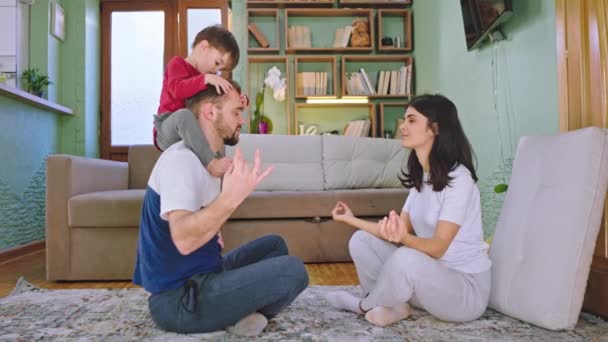 Na sala de estar pai e jovem mãe com seu pequeno filho fazendo ioga juntos enquanto sentado no chão eles passam tempo em casa — Vídeo de Stock