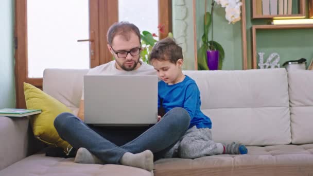 Carismático menino pequeno com seu pai se divertir juntos usando um laptop para jogar um jogo eles conversando juntos têm um relacionamento amigável — Vídeo de Stock