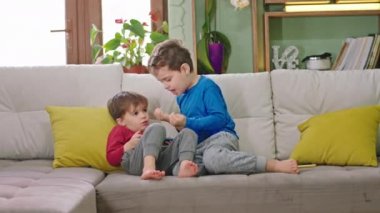 İki küçük kardeş evlerinde kanepede oturmuş akıllı telefonlarıyla oyun oynuyorlar sohbet ediyorlar ve birlikte iyi vakit geçiriyorlar.