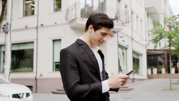 Przystojny, charyzmatyczny mężczyzna na środku ulicy, wpisujący coś, co ma na sobie w czarnym garniturze. Strzał na ARRI Alexa Mini — Wideo stockowe