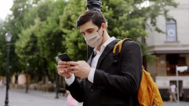 Covid-19 karantinasında koruyucu maskeli bir iş adamı sokağın ortasında telefonla bir şeyler yazıyor. ARRI Alexa Mini 'de çekilen