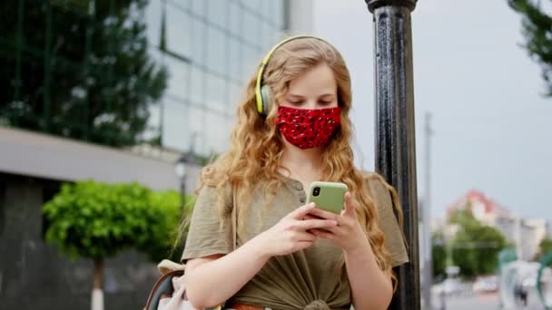 Na frente da câmera vestindo uma senhora máscara protetora com um cabelo comprido no meio da rua digitando algo na pandemia smartphone de Coronavirus. Tiro em ARRI Alexa Mini — Vídeo de Stock