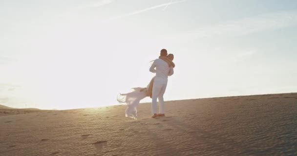 Pareja joven en medio de la playa al atardecer increíble abrazándose y sintiéndose enamorados, el hombre toma a la dama en el brazo y gira — Vídeo de stock