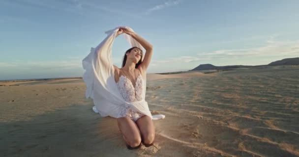 Zeer knappe jonge vrouw in witte jurk midden op het strand met wit zand. 4k — Stockvideo