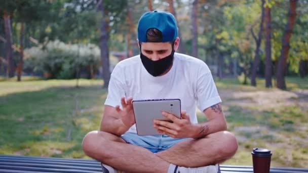 A Coronavírus világjárványában a diák srác kávét iszik, és védőmaszkot visel, amit online tanul a friss levegőn. — Stock videók
