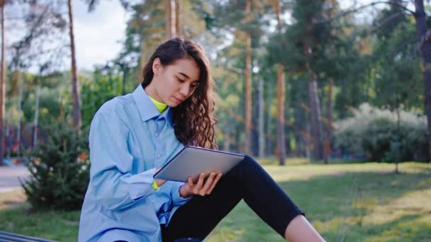 Молода жінка азіатська дивлячись у великий зелений парк, використовуючи електронний планшет, щоб набрати щось зосереджене вона дивиться через планшет — стокове відео
