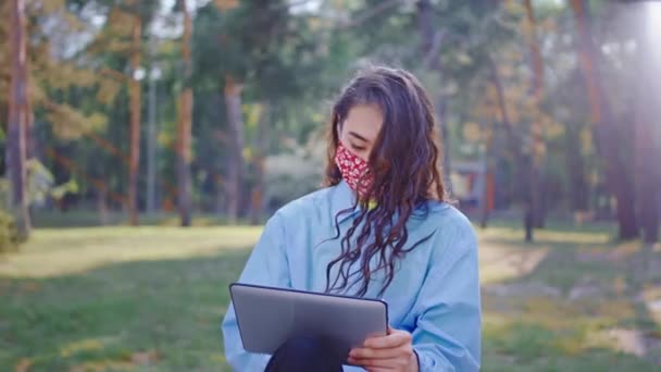 Nel parco pandemia di Coronavirus 2019 signora asiatica cercando utilizzando un tablet per lavorare online indossa maschera protettiva concentrata lei digitando qualcosa. — Video Stock