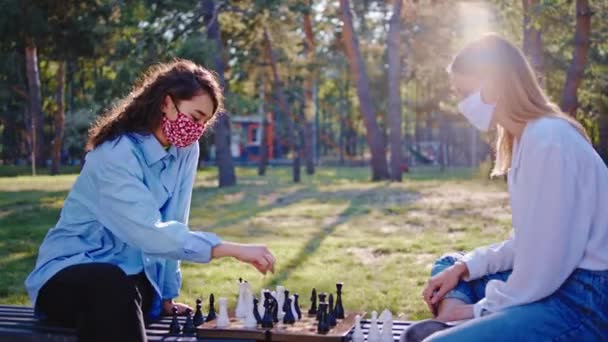 コロナウイルスの隔離されたカメラの前でチェスゲームで遊んで新鮮な空気で二人の友人多民族の女性 — ストック動画