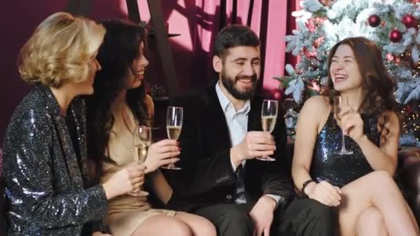 Atractivo grupo de damas y un chico sentado en el sofá en la fiesta de Navidad que socializar y beber un poco de vino espumoso — Vídeos de Stock