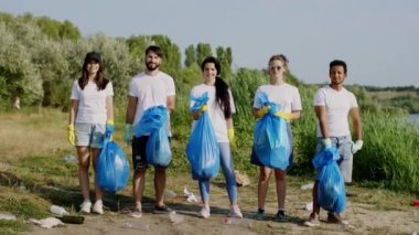 Sahilde temizlik yaptıktan sonra kameraların önünde poz veren çok ırklı gönüllüler ellerinde çöp dolu plastik torbalar tutuyorlardı. 4k