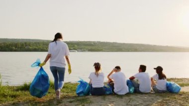 Genç gönüllülerden oluşan bir grup çöpü temizlemeyi bitirdikten sonra gölün kenarında oturup doğanın tadını çıkarıyor ve muhteşem göl manzarasına bakıyor.