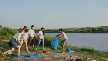 Güneşli bir günde, çok ırklı gönüllülerden oluşan bir grupta birlikte oynadıkları çöpleri temizlerken iyi vakit geçirin. Afro-Amerikan bir adam mavi plastik bir torba ve bir bayanla birlikte eğlenin.