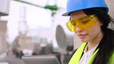 Çekici bayan mühendis, elinde dijital tabletle binanın çatısında gülümseyerek doğrudan kameraya bakıyor.