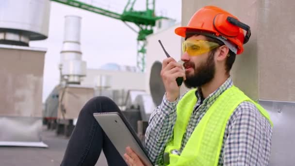 Closeup to the camera good looking man architect on the top of construction site using the digital tablet and ration to hav a conversation with other specialists from the site he using a digital — Stock Video