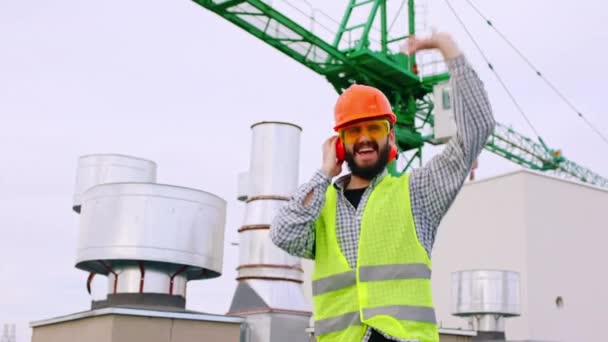 カリスマ的なエンジニアの男が踊り、建設現場の上で興奮して、彼はカメラの前で安全のためにすべての機器を身に着けています — ストック動画